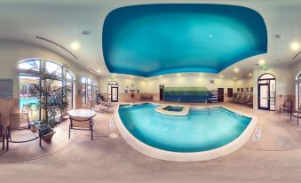 a large indoor pool with a blue ceiling and white base , surrounded by lounge chairs at Courtyard Houma