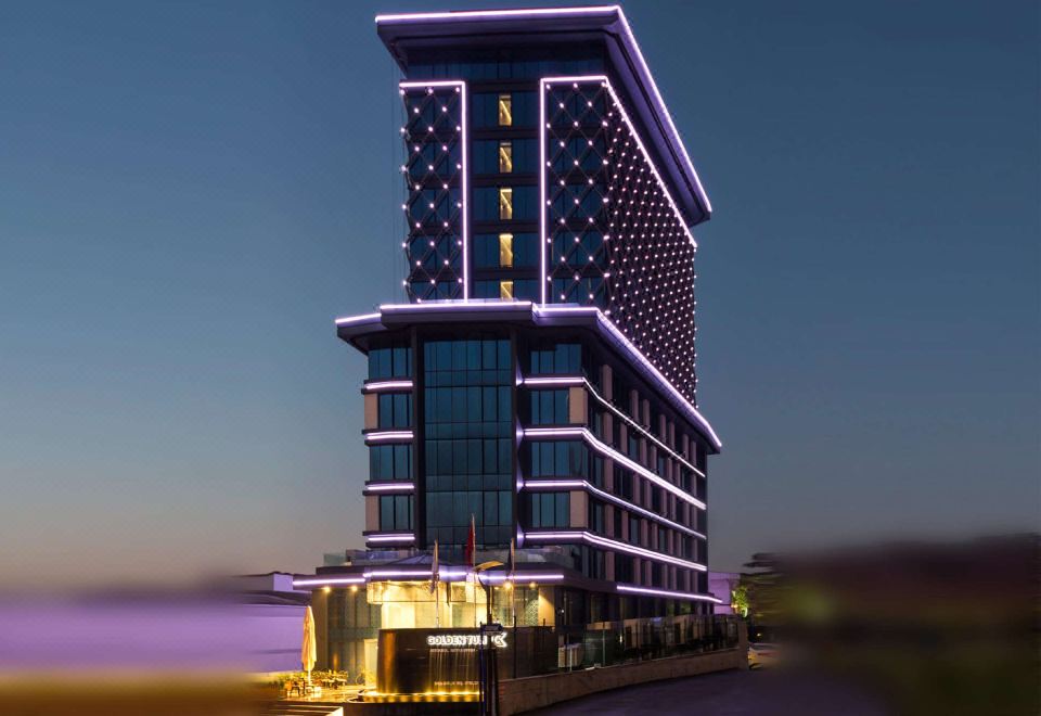 a tall building with a unique design , lit up with purple and blue lights against the dark night sky at Golden Tulip Istanbul Bayrampasa