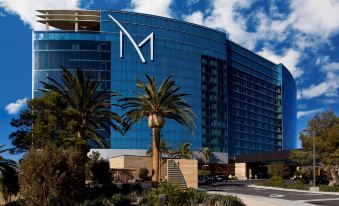 "a large blue building with a "" m "" logo prominently displayed on the front , surrounded by palm trees and other plants" at M Resort Spa & Casino