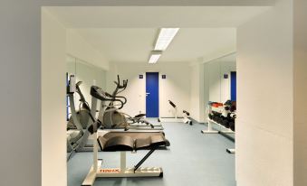 a gym with various exercise equipment , including a treadmill and stationary bike , in a white - walled room at Bellevue Hotel