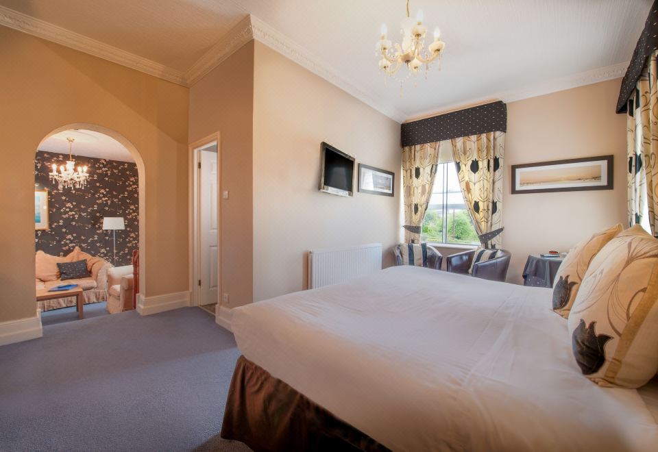 a large bedroom with a king - sized bed , a chandelier hanging from the ceiling , and a television mounted on the wall at Best Western New Holmwood Hotel