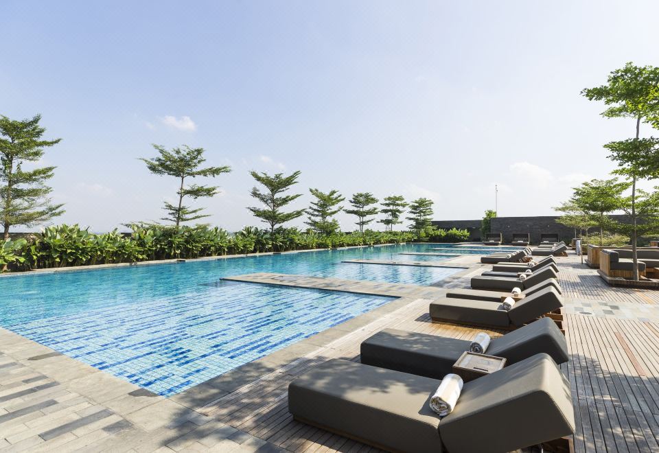 a large outdoor swimming pool surrounded by lounge chairs , with palm trees in the background at Alila Solo