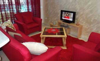 a living room with red chairs and a wooden coffee table in front of a television at Rahma