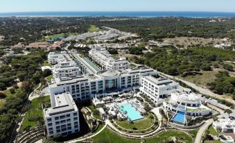 aerial view of a large white building with a swimming pool , surrounded by trees and grass at Conrad Algarve