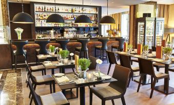 a restaurant with several dining tables and chairs , along with a bar area in the background at Steigenberger Hotel Koln