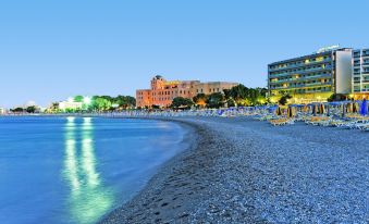 a beautiful beach with clear blue water , sandy shoreline , and illuminated buildings in the background at Mediterranean Hotel