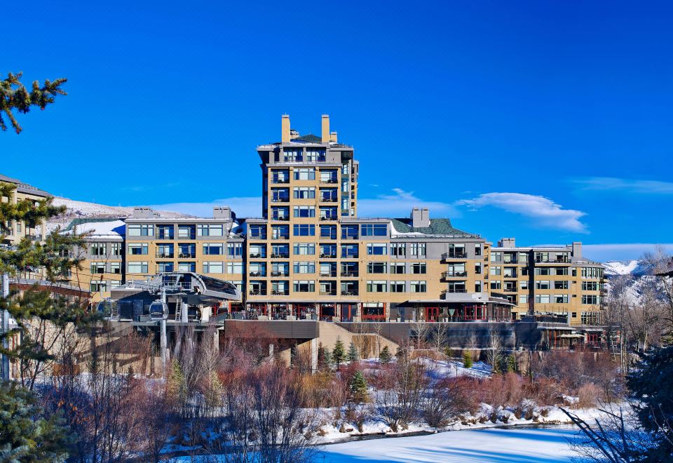 a large hotel building surrounded by snow - covered trees and a body of water , creating a picturesque winter scene at The Westin Riverfront Resort & Spa, Avon, Vail Valley