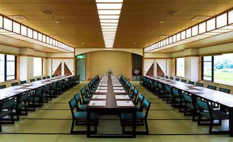 a long dining table with blue chairs is set up in a large , empty room at Yufuin Hotel Shuhokan