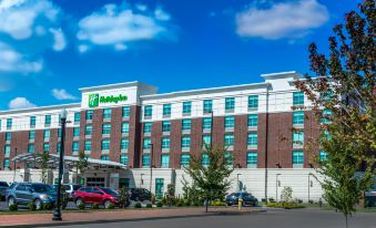 a holiday inn hotel with a red and white facade , surrounded by trees and parked cars at Holiday Inn Owensboro Riverfront