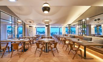 a modern restaurant with wooden tables and chairs , pendant lights , and large windows overlooking the city at Cascade Wellness Resort