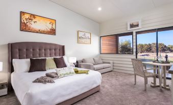 a large bed with a white comforter and brown pillows is in a room with two windows , a couch , and framed pictures on the wall at The Swan Valley Retreat