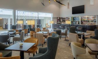 a large , modern lounge area with multiple tables and chairs , a television on the wall , and multiple chairs facing each other at DoubleTree by Hilton London Heathrow Airport