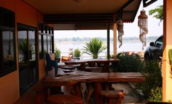 an outdoor dining area with wooden tables and chairs , overlooking a body of water from a building at Baan Rim Khong Resort