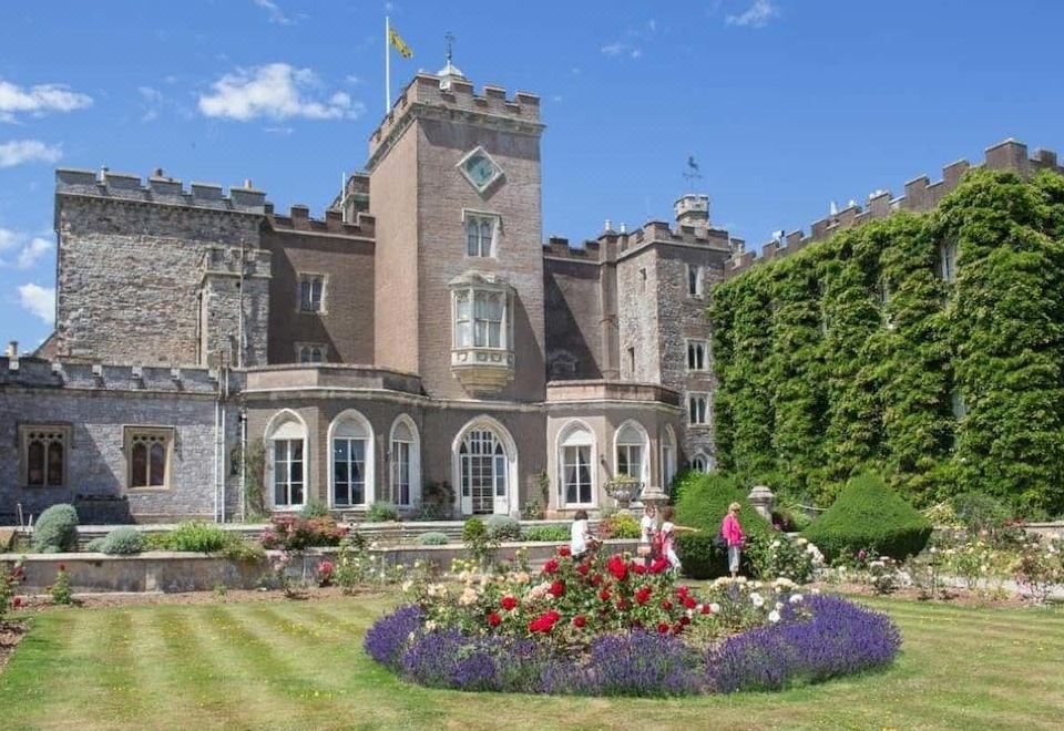 a large stone castle with a clock tower and a garden filled with colorful flowers at Hampton by Hilton Exeter Airport