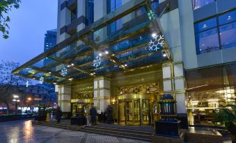 At night, a hotel entrance is adorned with an illuminated clock above its glass front entry at Central Hotel Shanghai