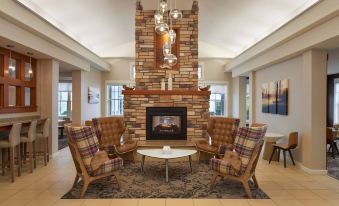 a modern living room with a brick fireplace , wooden chairs , and a chandelier hanging from the ceiling at Residence Inn Gravenhurst Muskoka Wharf