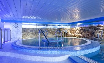 an indoor swimming pool with a stone wall and blue lights , surrounded by a spa area at Hotel Olympia Valencia