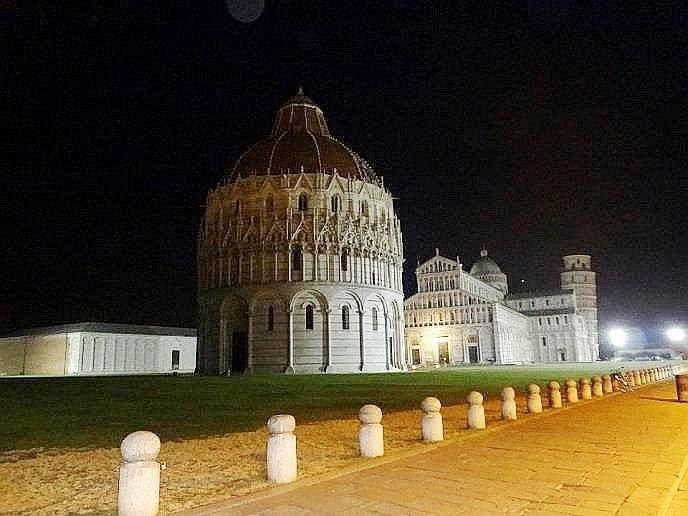 a nighttime view of the baptistery , a historical monument in pisa , italy , with its distinctive dome and surrounding white columns illuminated by lights at Hotel Leonardo