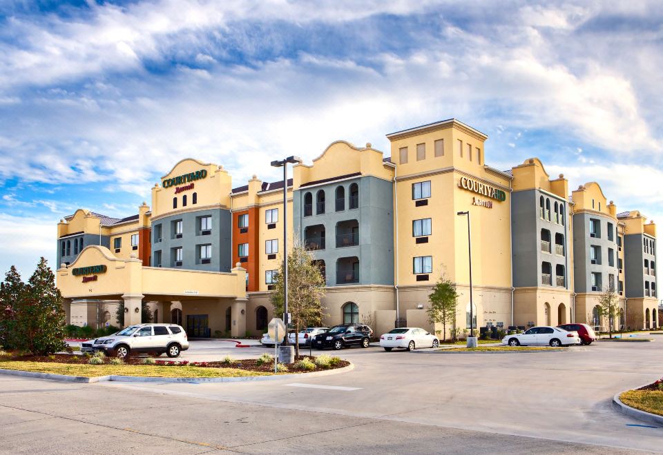 a large hotel with a parking lot in front of it , surrounded by cars and trees at Courtyard Houma