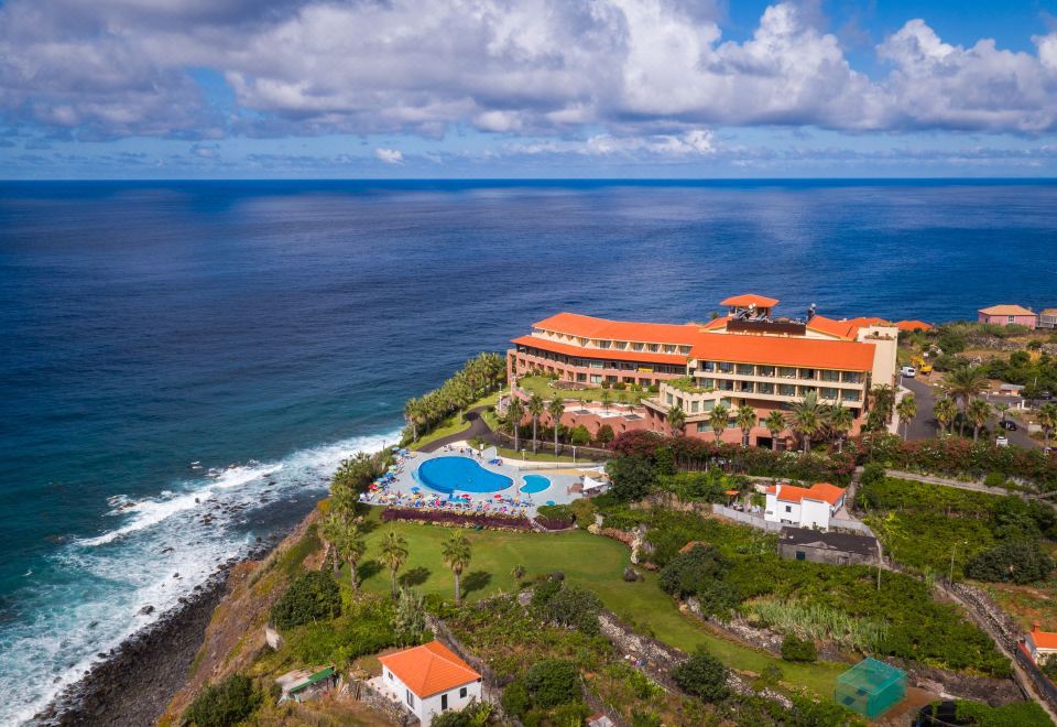 aerial view of a large hotel surrounded by ocean and grass , with a swimming pool visible in the background at Monte Mar Palace Hotel