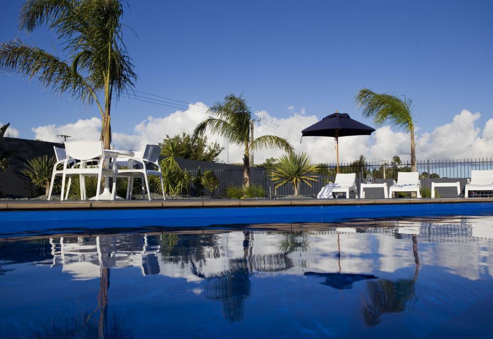 a beautiful swimming pool surrounded by palm trees , umbrellas , and lounge chairs under a clear blue sky at Motel Oasis