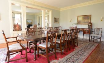 a large dining room with a long wooden table surrounded by chairs , and a red rug on the floor at Woodville Bed and Breakfast