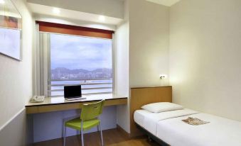 A bedroom is equipped with a bed, desk, and chair positioned near the window at Ibis Hong Kong North Point