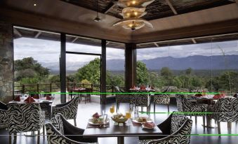 a dining room with a table set for breakfast , surrounded by chairs and a view of the mountains outside the window at The Serai Bandipur