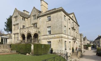 a large stone mansion with a grassy area in front of it , surrounded by trees at The Painswick