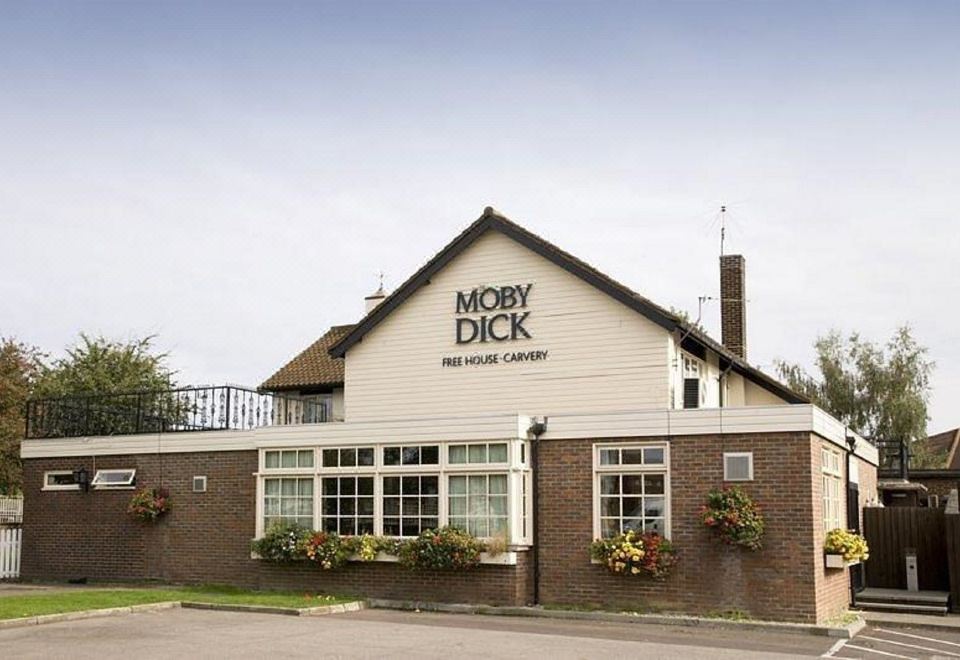 "a brick building with the words "" moby dick "" written on it , surrounded by greenery and flowers" at Premier Inn London Romford West