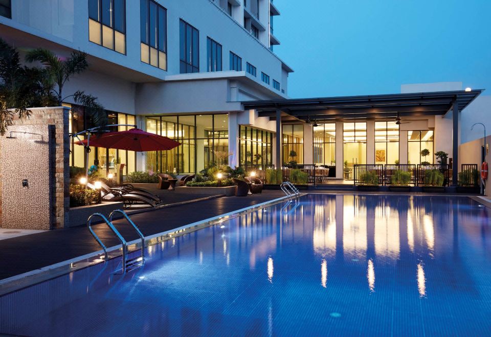 a large swimming pool is surrounded by lounge chairs and a building with glass windows at Hilton Garden Inn Puchong