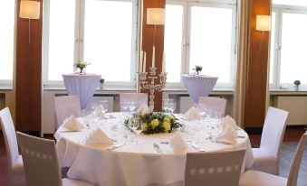a well - decorated dining room with a round table set for a formal event , surrounded by white chairs and adorned with centerpieces at Hotel am Rhein