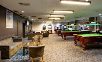 a spacious , well - lit room with multiple billiard tables and couches , where people are playing video games at Nightcap at Westside Hotel