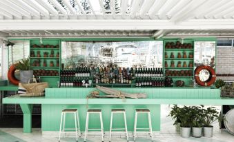 a bar with green walls , white stools , and a large window , offering a view of various bottles and wine glasses at Watsons Bay Boutique Hotel