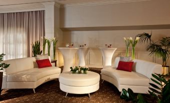 a room with white furniture and a round table in the center , surrounded by potted plants at Holiday Inn Laval - Montreal