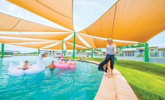 a group of people , including a woman and a man , are swimming in a pool with inflatable flamingos at Club Tropical Resort Darwin