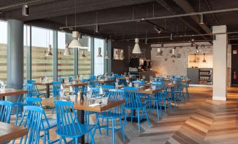 a modern restaurant with wooden tables and blue chairs , large windows , and hanging lights , creating an inviting atmosphere at Best Western Plus Hotel Amstelveen