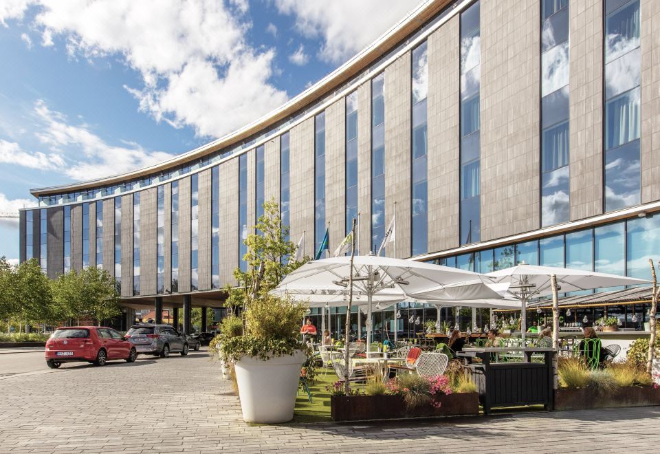 a modern building with a curved glass facade and several umbrellas on the ground floor at Radisson Blu Hotel Uppsala