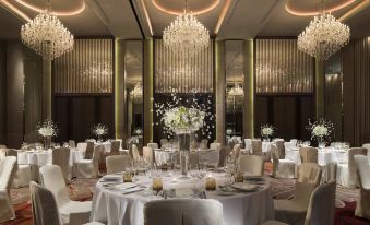 A ballroom is set up for an event with round tables and chandeliers hanging over the main table at Bangkok Marriott Hotel Sukhumvit