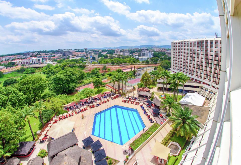 a large swimming pool surrounded by lounge chairs and umbrellas , with a city skyline visible in the background at Transcorp Hilton Abuja