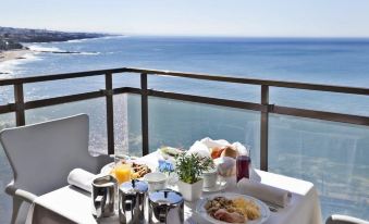 a breakfast table set up on a balcony with a view of the ocean , surrounded by chairs and a dining table at Hotel Estoril Eden