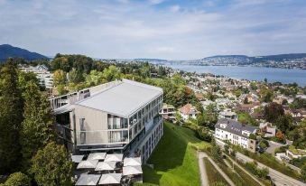 a modern building with a large glass roof is surrounded by greenery and overlooks a city at Belvoir Swiss Quality Hotel