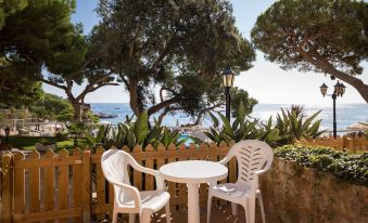 a white table and chairs are set up on a patio overlooking the ocean , with trees in the background at Htop Caleta Palace #HtopBliss