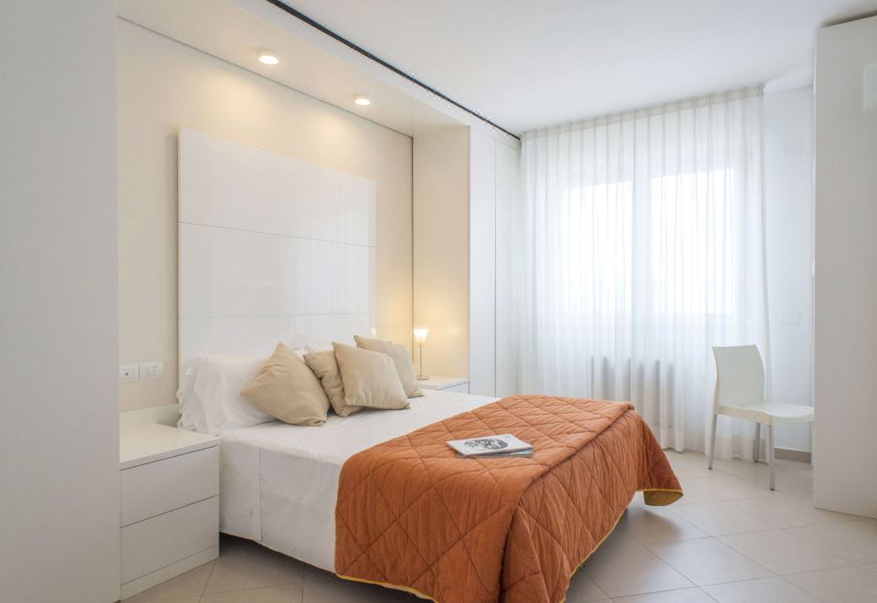 a large white bed with a wooden headboard and orange blanket is in a room with white walls at Nautilus