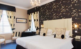 a large bed with white sheets and black headboards is in a room with a chandelier , curtains , and artwork on the wall at Best Western New Holmwood Hotel