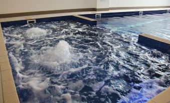 a large indoor swimming pool filled with water , surrounded by a white wall and a blue tiled floor at Pegasus Apart'Hotel