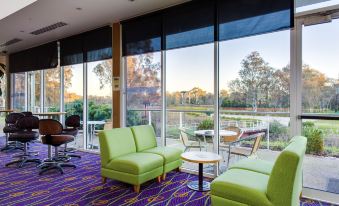 a room with green couches and chairs arranged in front of a large window , overlooking a grassy field at Thurgoona Country Club Resort