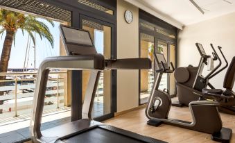 a well - equipped gym with various exercise equipment , including treadmills and weight machines , positioned near large windows that offer views of the outside at Riviera Marriott Hotel la Porte de Monaco