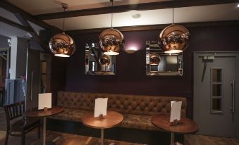 a modern bar with a wooden floor , brown couches , and several hanging copper lights , creating an inviting atmosphere at Richmond Park Hotel