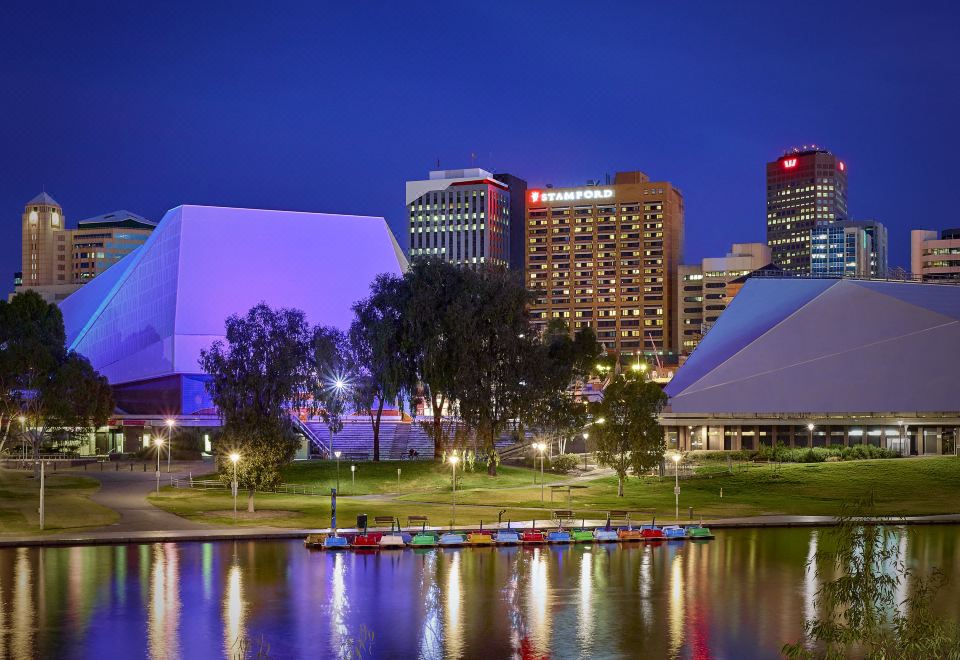 a city skyline at night , with tall buildings illuminated and a river reflecting the lights in the water at Stamford Plaza Adelaide